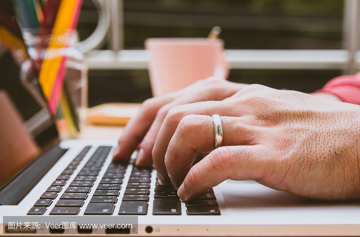 男人的手戴着结婚戒指,把键盘放在网上打字,工作在电脑笔记本电脑上,在家喝杯咖啡在办公室。